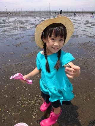 麦わら帽子の子どもが採った貝を見せる様子