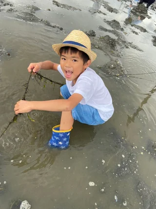麦わら帽子をかぶって干潟にしゃがむ子ども