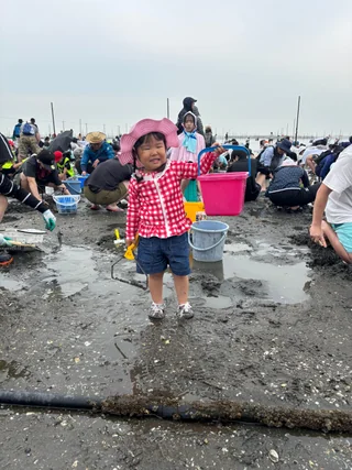 ピンクのバケツを持って干潟に立つ子ども