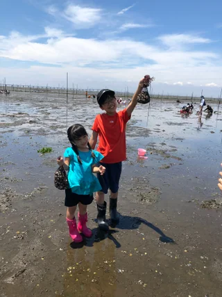 貝の入った網袋を掲げる子ども2人