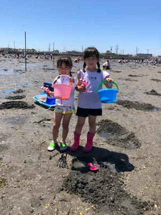 干潟でバケツを手に並ぶ子ども2人
