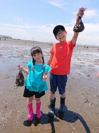 貝の入った網袋を持って並ぶ子ども2人