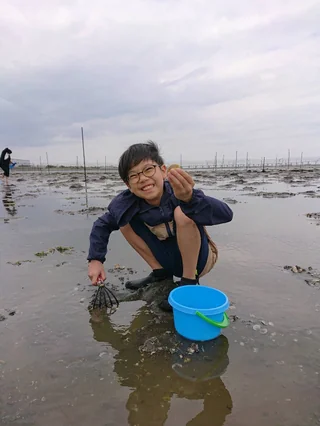 青いバケツのそばで貝を探す来場者