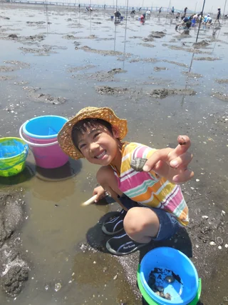 バケツや潮干狩り道具のそばに座る子ども
