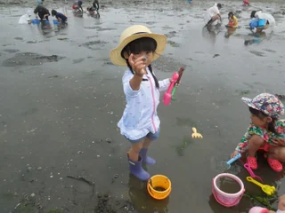 黄色いバケツのそばで貝を見せる子ども