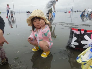 麦わら帽子をかぶって貝を見せる子ども
