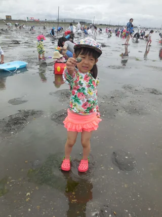 干潟で採った貝を見せる花柄の服の子ども