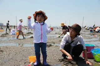 干潟で片手を上げる帽子姿の子ども