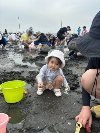 緑のバケツのそばで貝を探す幼児