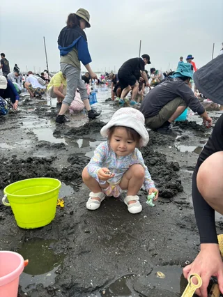 周りの人と一緒に干潟にしゃがむ幼児