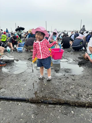 ピンクのバケツを持つ子どもと潮干狩りの来場者