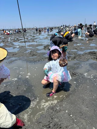 潮干狩りの道具のそばで干潟に座る子ども