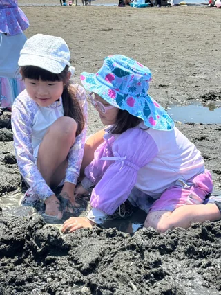 並んで干潟を掘る帽子姿の子ども2人