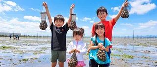 貝の入った網袋を掲げて笑顔を見せる子どもたち